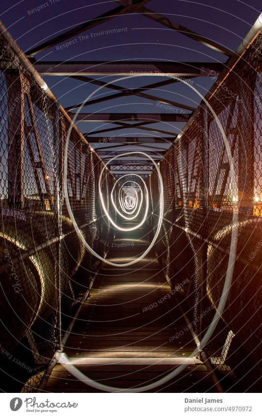 Torch light twirl on industrial footbridge. Industrial Bridge Footbridge Night torch light Abstract Swirl Spiral twist Circular pipes steel mesh Light