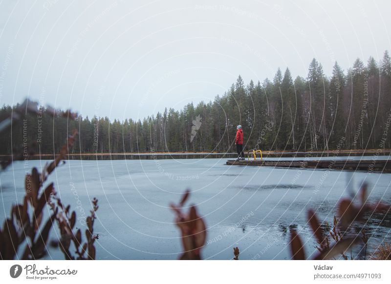 Explorer stands at the end of a pier, breathing fresh air, in the rain at Lake Pieni-Vimpeli near the town of Kajaani, Kainu region, Finland. The last days of autumn. Discovering beautiful places