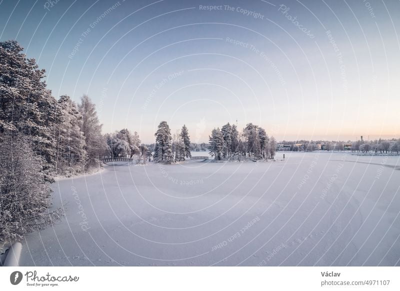 Frosty morning in the Finnish town of Kajaani in the north of the country in the Kainu region. A view of the frozen Kajaaninjoki river and the snowy forest near the river. Sunrise