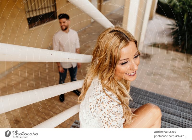 Young woman sitting on stairs against smiling man looking with interest on street couple trendy piercing cheerful girlfriend boyfriend fence exterior style