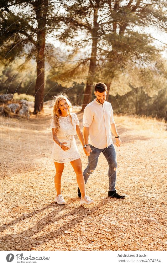 Couple holding hands and smiling while walking against green forest in evening couple happy park romantic love stroll girlfriend boyfriend date countryside