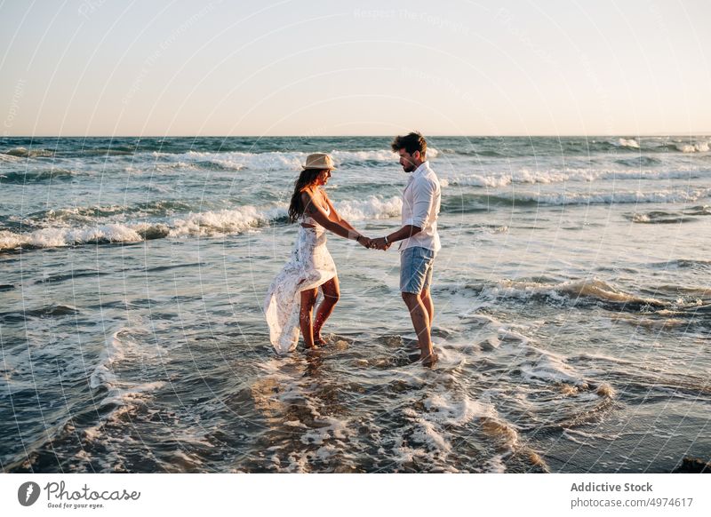 Affectionate couple standing on ocean waves holding hands on sunset sea summer in love sunlit enamored honeymoon intimacy amorous dating romantic tenderness