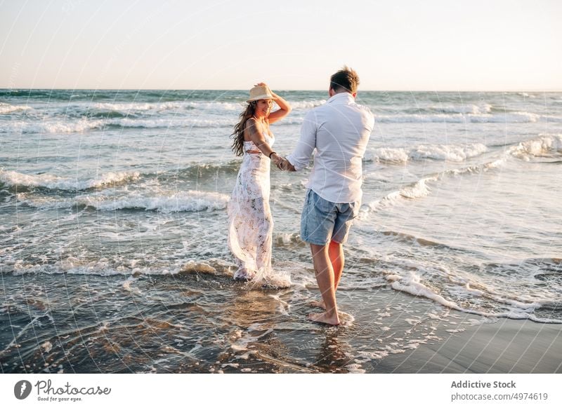 Affectionate couple standing on ocean waves holding hands on sunset sea summer in love sunlit enamored honeymoon intimacy amorous dating romantic tenderness