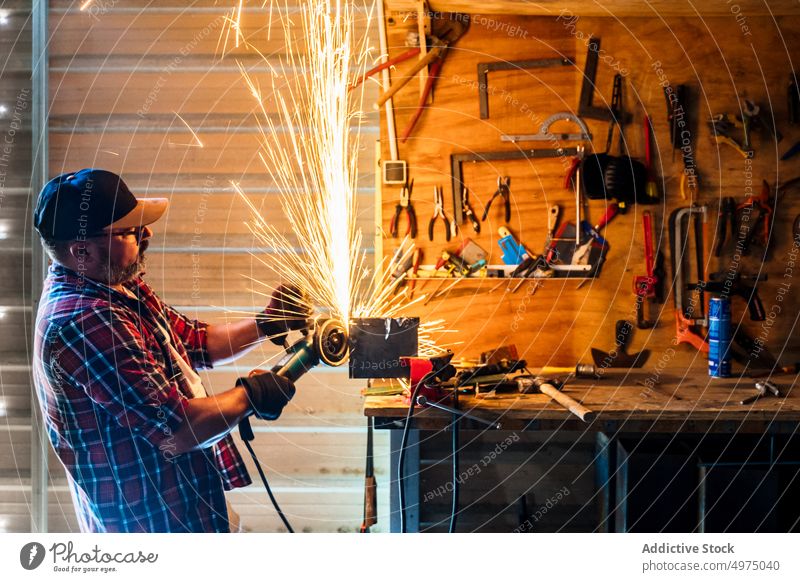 Male cutting piece of metal in modern workshop man angle grinder spark worker equipment using workplace instrument mechanic craftsman process industry garage