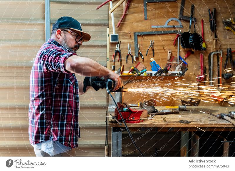 Male cutting piece of metal in modern workshop man angle grinder spark worker equipment using workplace instrument mechanic craftsman process industry garage