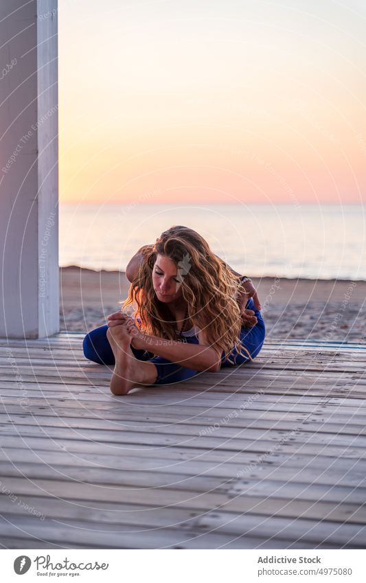 Flexible woman doing yoga at seaside during sunrise pose crescent lunge terrace tranquil sportswear practice wooden anjaneyasana serene healthy harmony calm