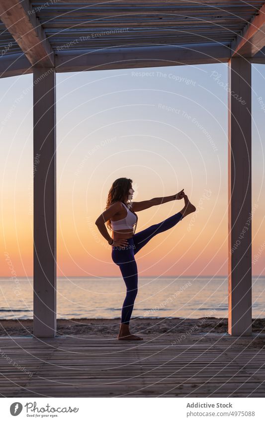 Flexible woman doing yoga at seaside during sunrise pose terrace tranquil sportswear practice wooden anjaneyasana serene healthy harmony calm dawn peaceful