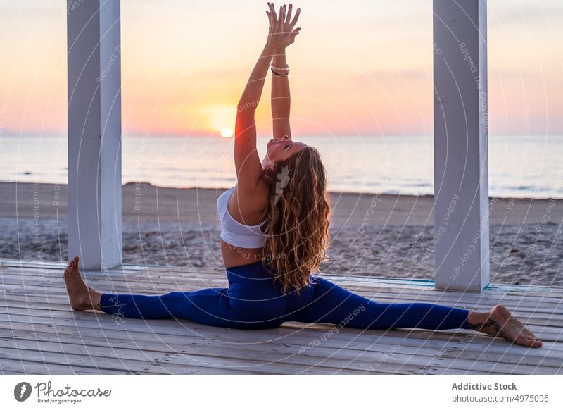 Flexible woman doing yoga at seaside during sunrise pose crescent lunge terrace tranquil sportswear practice wooden anjaneyasana serene healthy harmony calm