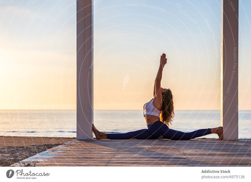 Flexible woman doing yoga at seaside during sunrise pose crescent lunge terrace tranquil sportswear practice wooden anjaneyasana serene healthy harmony calm