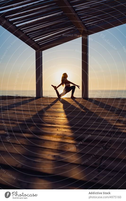 Tranquil woman doing yoga in Warrior pose during sunrise warrior seaside practice tranquil silhouette dawn wooden terrace healthy harmony relax asana