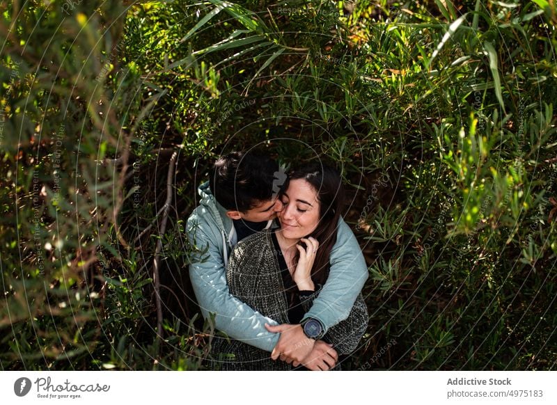 Romantic young ethnic couple cuddling amidst lush green trees in nature hug bite eyes closed romantic love affection park relationship happy embrace girlfriend