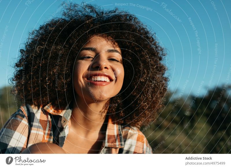 Charming black woman with curly hair smiling on street hipster sunset afro hairstyle content charming smile checkered shirt female ethnic african american enjoy