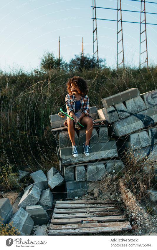 African American woman with penny board sitting on stones on the street summer skater cool millennial afro trendy tranquil hipster sunny female ethnic