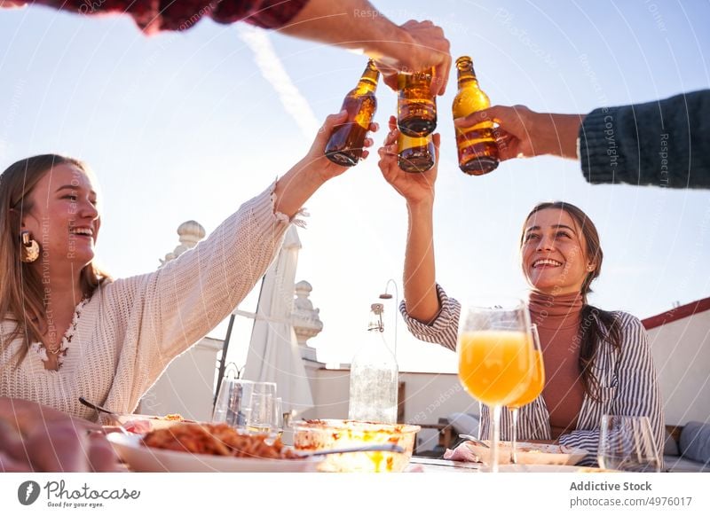 Joyful friends clinking beer bottles and having lunch on terrace content cheers together toast celebrate alcohol vertical booze party drink gather cheerful