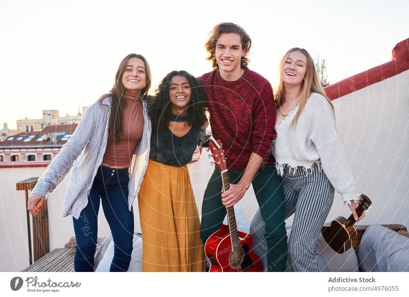 Smiling diverse friends with guitar gathering on terrace rooftop toothy smile musician cheerful hug together young fun instrument ukulele veranda relationship