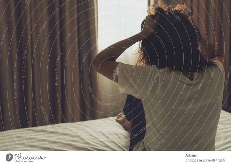 World Mental Health Day concept. Rear view of angry woman put hand on head and pulling hair. Mental illness woman sit on bed in bedroom. Woman with mental health problems. Stressed and nervous person.