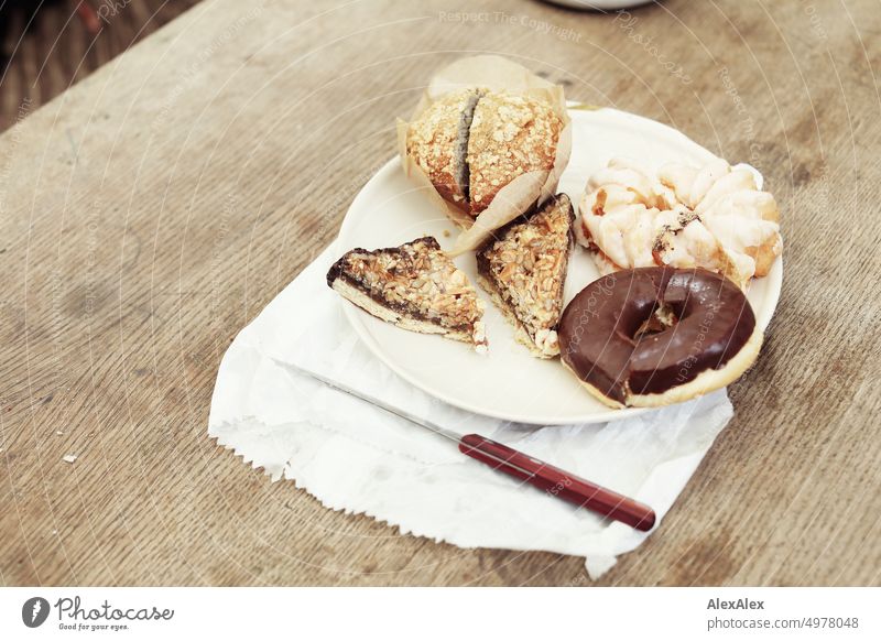 Plate with cake - muffin - nut corner - donut and spritz cake - stands on a wooden table on a paper bag. Table Wooden table Cake Nut corner doughnut Muffin