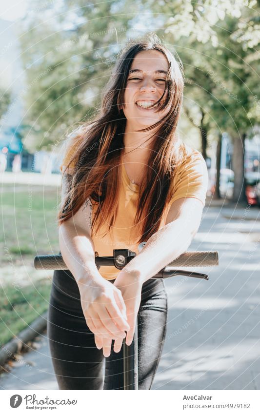 Portrait of young woman smiling leaning on an electric scooter in the city.Resting after an entire day of visiting all places of interest.Having fun riding public,eco and rechargeable transport.