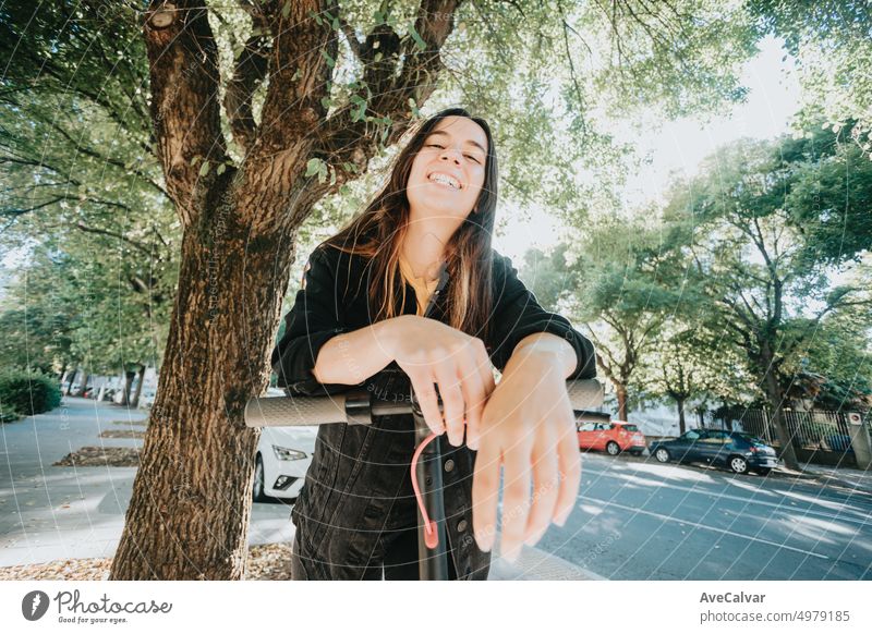 Portrait of young woman smiling leaning on an electric scooter in the city.Resting after an entire day of visiting all places of interest.Having fun riding public,eco and rechargeable transport.