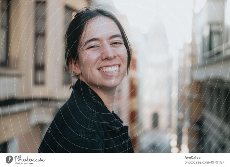 Portrait of young woman smiling at camera in urban colorful scenery in the city. Cheerful, happy and carefree. New style life. Casual clothes in daily routine