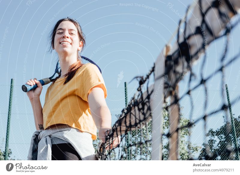 Young girl beginner tennis player waiting leaning on the tennis net to start the match with big smile.Holding a racket excited for learn a sport.New hobby and healthy life and style,happy and nervous