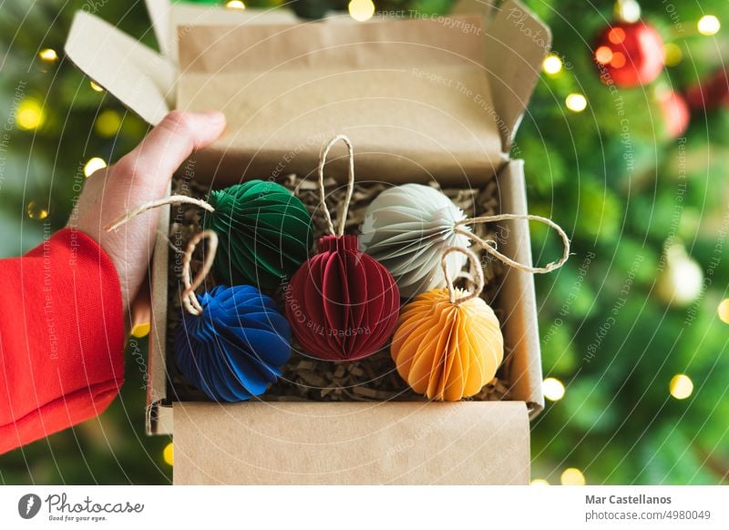 Hand holding box with Christmas ornaments. Colored paper balls. Copy space. cardboard hand open lights copy homemade rope handmade 5 close up part of body show