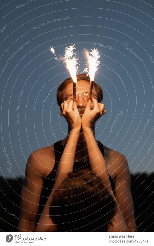 This man is ready to celebrate. With all these fireworks almost burning his eyes he is having fun dangerously. A wild man enjoys pyrotechnics. Fireworks