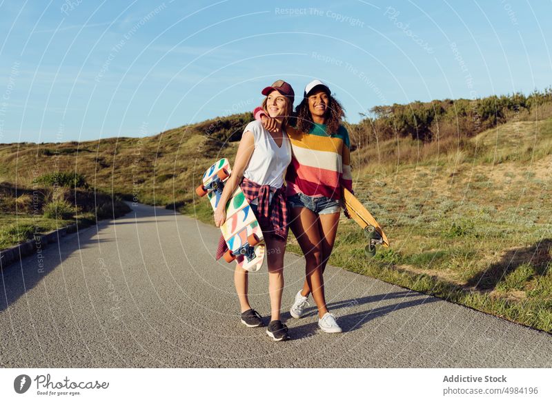 Women friends walking down the road holding skate boards women portrait skateboard skater countryside fun woman beautiful young trendy stylish skateboarder