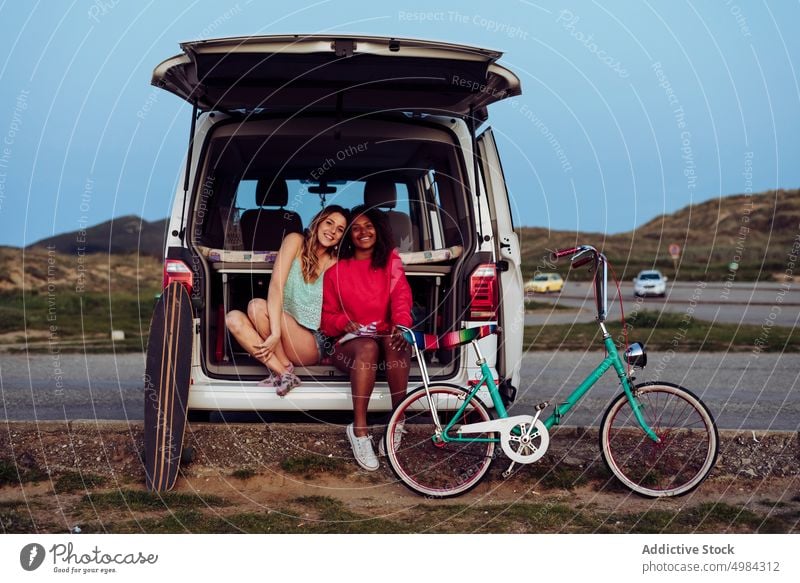 Cheerful women sitting on trunk of van eating popcorn caravan car journey trip transportation vacation adventure travel summer camper recreation active leisure