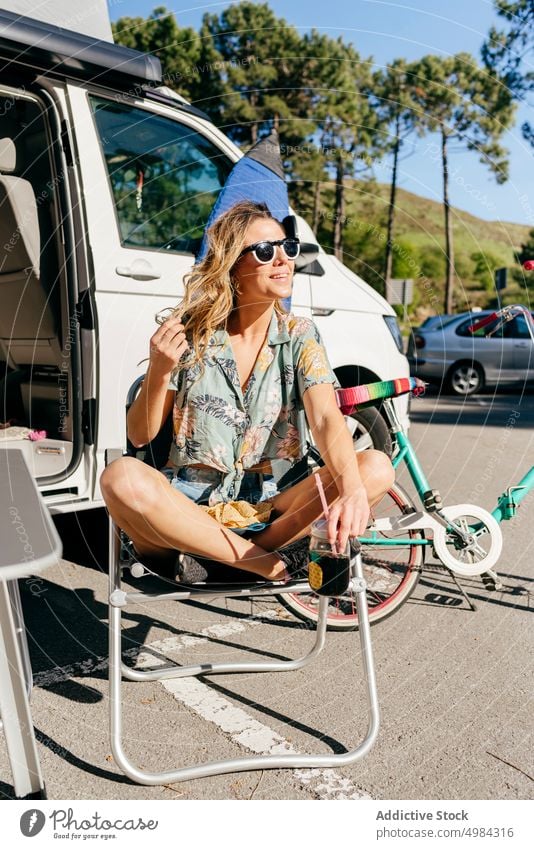 Cheerful woman enjoying a juice while sitting out of caravan in camping journey trip transportation vacation adventure travel summer camper recreation leisure