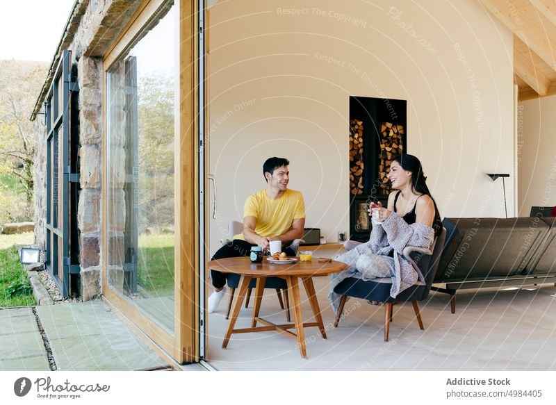 Young smiling woman and man drinking from cups and sitting on chair near window couple hispanic room mug young big beautiful happy cheerful court attractive