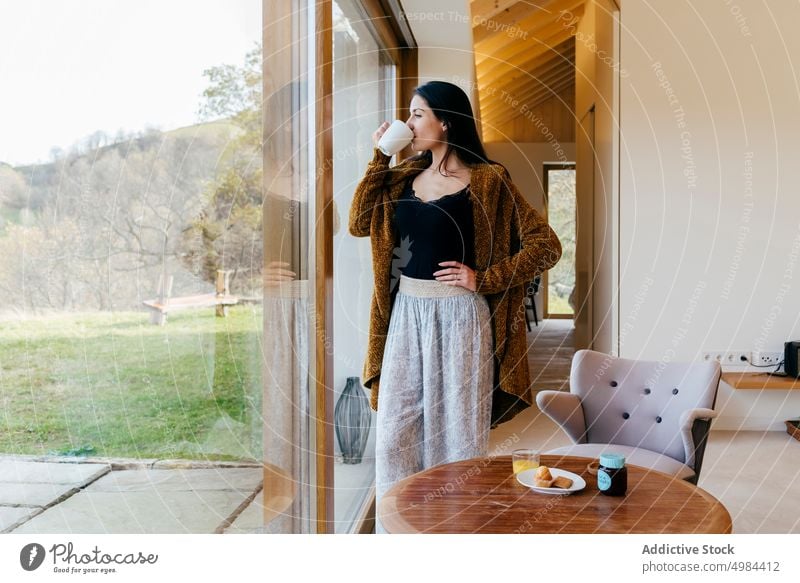 Young woman with cup near window in room hispanic lady attractive mug drink young big beautiful court cozy home rest relax beverage liquid lovely charming