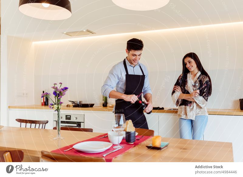 Man opening wine bottle near woman with a glass in kitchen couple drinking pinafore pouring beverage plate table dinning young dinner feast food dish