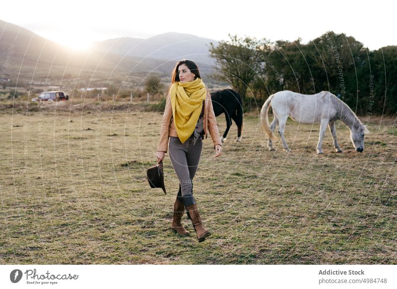 Woman walking on field among horses ranch animal romantic harmony countryside horseback lifestyle nature equine smile meadow equestrian content recreation scarf