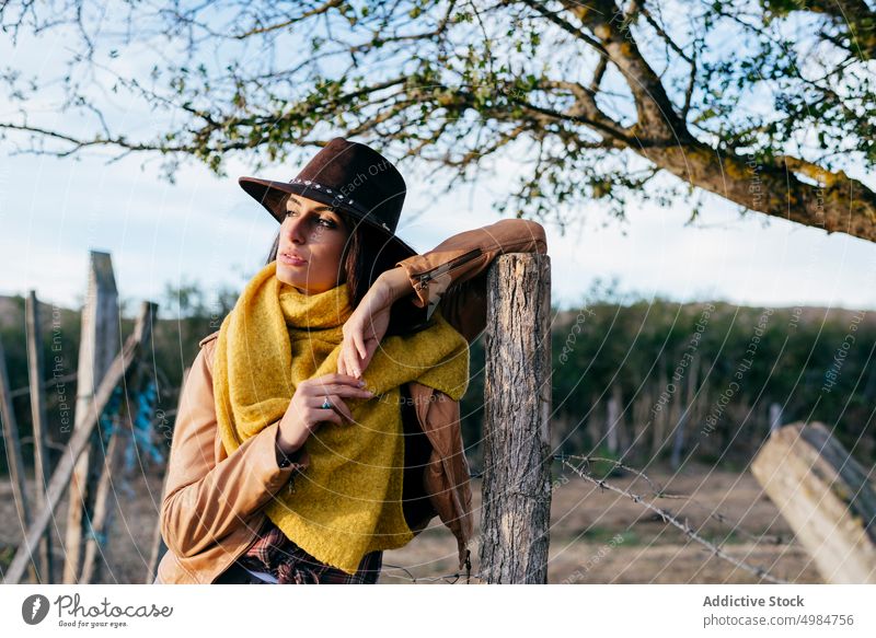 Stylish woman in scarf and cowboy hat beautiful style ranch nature standing cowgirl trendy thoughtful dreaming brunette harmony fence young landscape wood