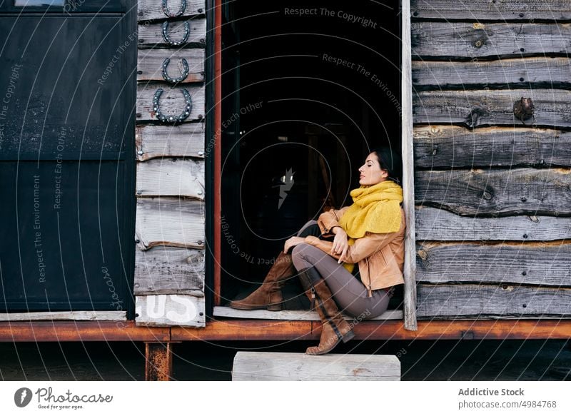 Sensual brunette sitting on house of ranch style porch rural boots freedom outdoors young harmony scarf home idyllic scenic exterior building estate attractive