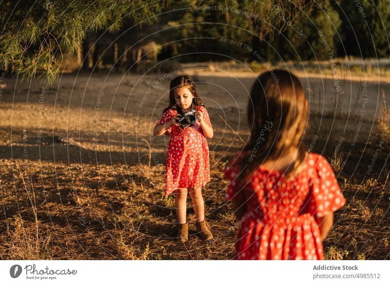 Girl taking photo of little sister in meadow girl friendship summer field nature camera photography happy beautiful technology adorable red child enjoyment