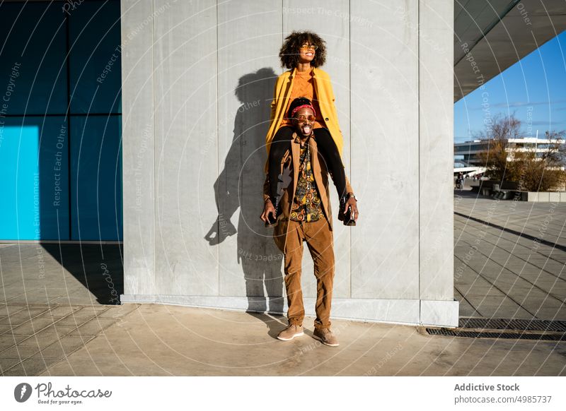 Cool back man carrying girlfriend on shoulders in city couple street style trendy urban fashion tall colorful ethnic black african american happy together