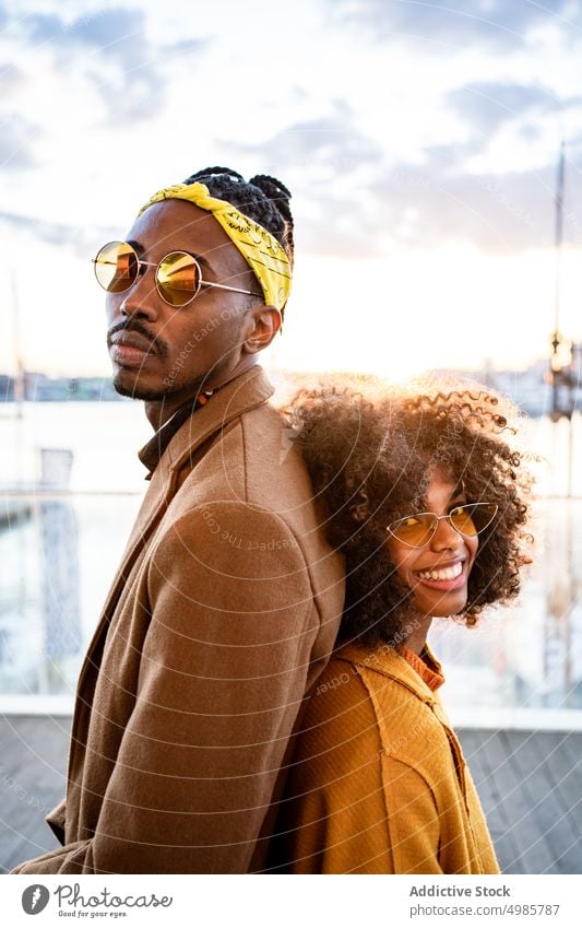 Stylish black couple in coats on city promenade pier trendy urban colorful autumn style laugh ethnic african american fashion afro dreadlocks hairstyle yellow