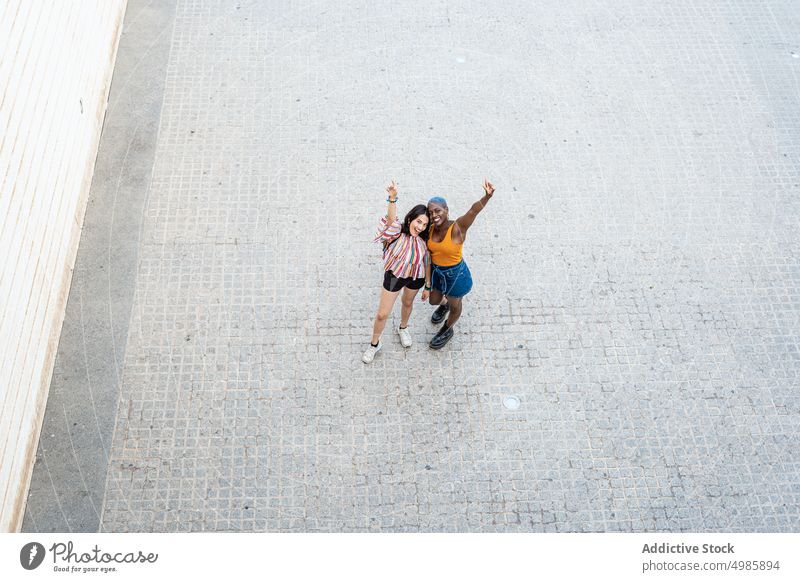 Stylish multiethnic couple of lesbian women in city cool urban style lgbt smile raised arm cheerful positive same sex girlfriend street multiracial diverse