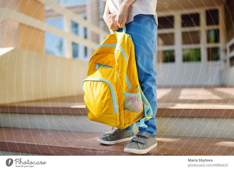 Little student with a backpack on the steps of the stairs of school building. Close-up of child legs, hands and schoolbag of boy standing on staircase of schoolhouse.Back to school concept.