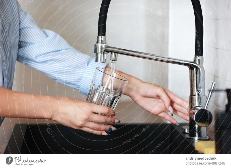 Woman filling drinking glass with tap water on the kitchen. Concept of clean drinking tap water at home. Pouring fresh drink. Water quality check concept. The concept of saving, problems with water