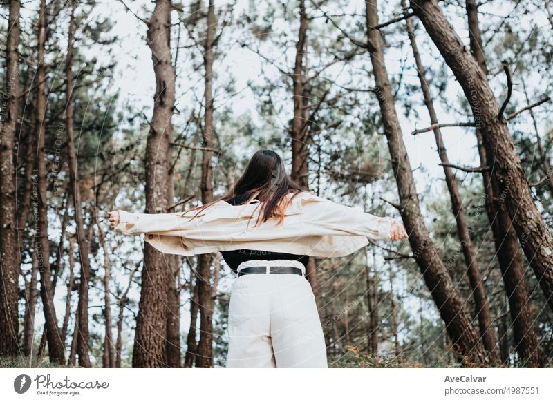 Young woman dancing and moving free in the middle of a forest.Back shot.Liberty and freedom concept person carefree turning happiness arm confidence emotion