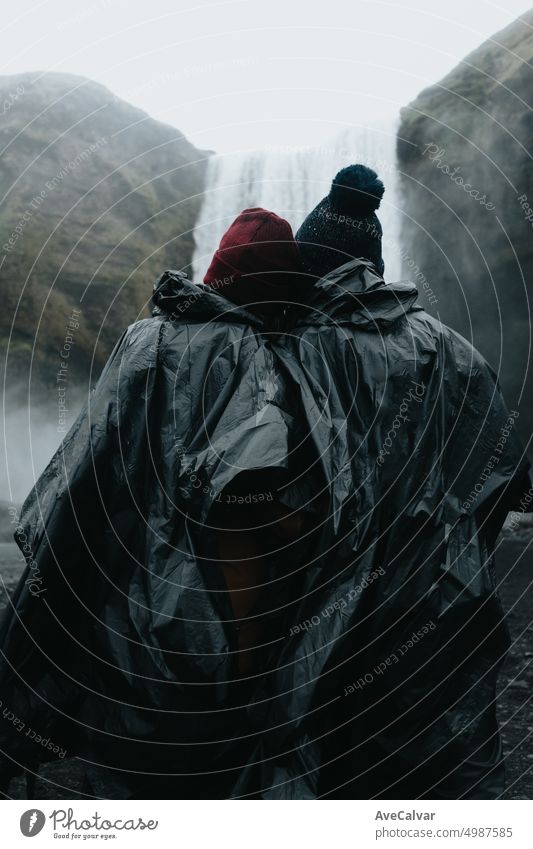 Young travelers couple in front of massive skofagoss waterfall at Iceland Island during a rainy day person woman popular smiling family happy affectionate awe