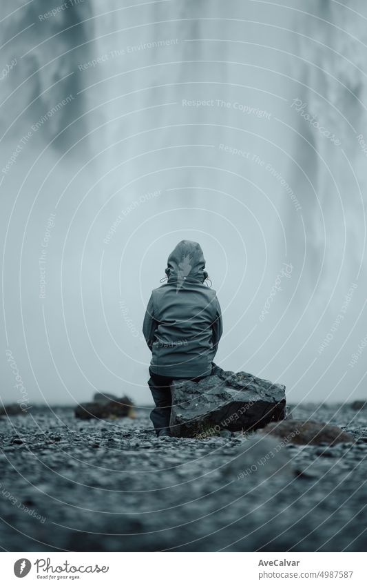 Young traveler in front of massive skofagoss waterfall at Iceland Island during a foggy rainy day person woman back female achievement awe dance drive elegance