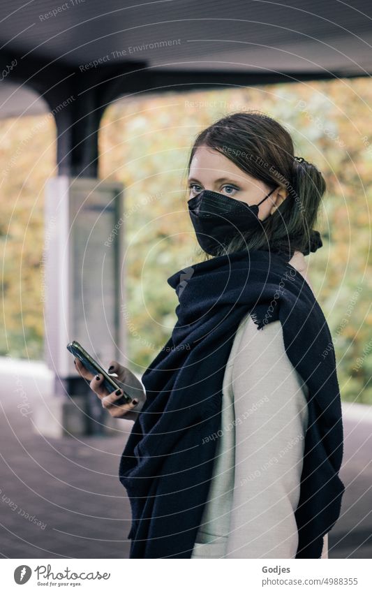 Young woman standing on a platform with smartphone in hand and wearing mouth guard | Corona thoughts Woman Train station SBahn Railroad Exterior shot