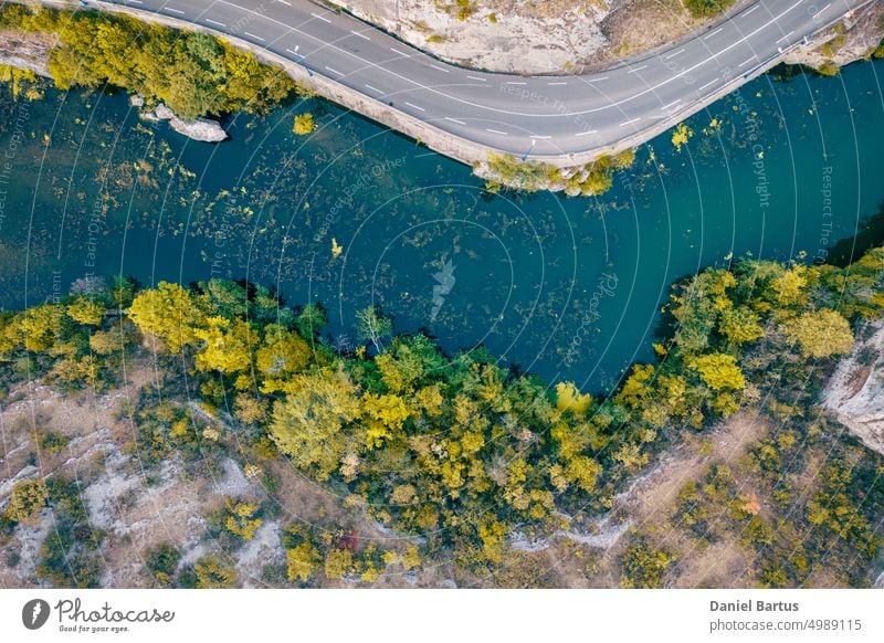 A road on a mountain slope overlooking a river with colorful vegetation and trees on the edge of the slope. Drone flight view. Background autumn landscape