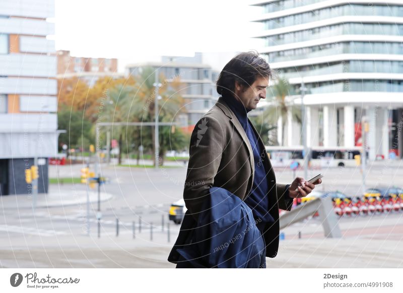 Confident man looking to mobile phone while walking on a street, man in suite walking on a street wall with copy space person business businessman message city