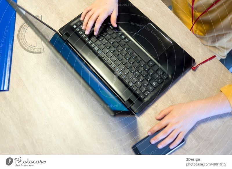 Hands of a young boy typing on a laptop keyboard over a rustic wooden table. Laptop exam homework school student hand technology person desk studying phone