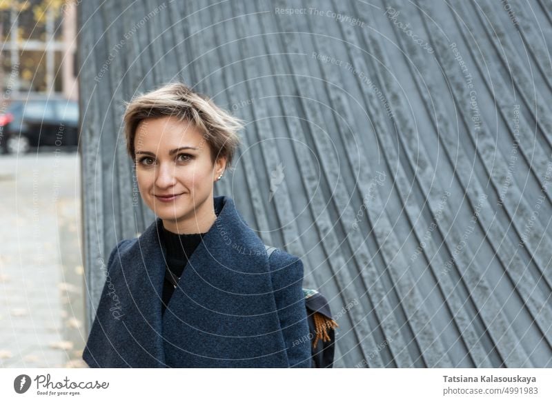 Short-haired blonde in coat smiles standing in the city woman fall autumn chilly Autumnal Urban Urban scene female adult Blond short hair Beautiful joy